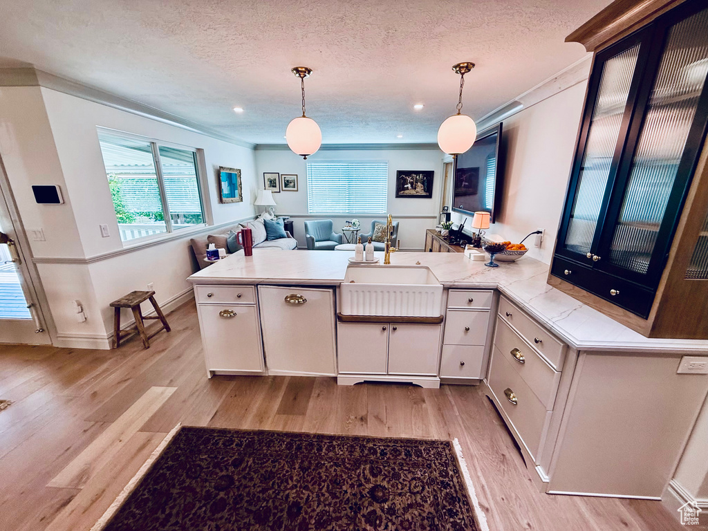 Kitchen with a sink, light wood-style flooring, a peninsula, hanging light fixtures, and a textured ceiling