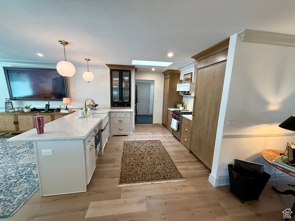 Kitchen featuring stainless steel range, a peninsula, light wood-style flooring, glass insert cabinets, and decorative light fixtures