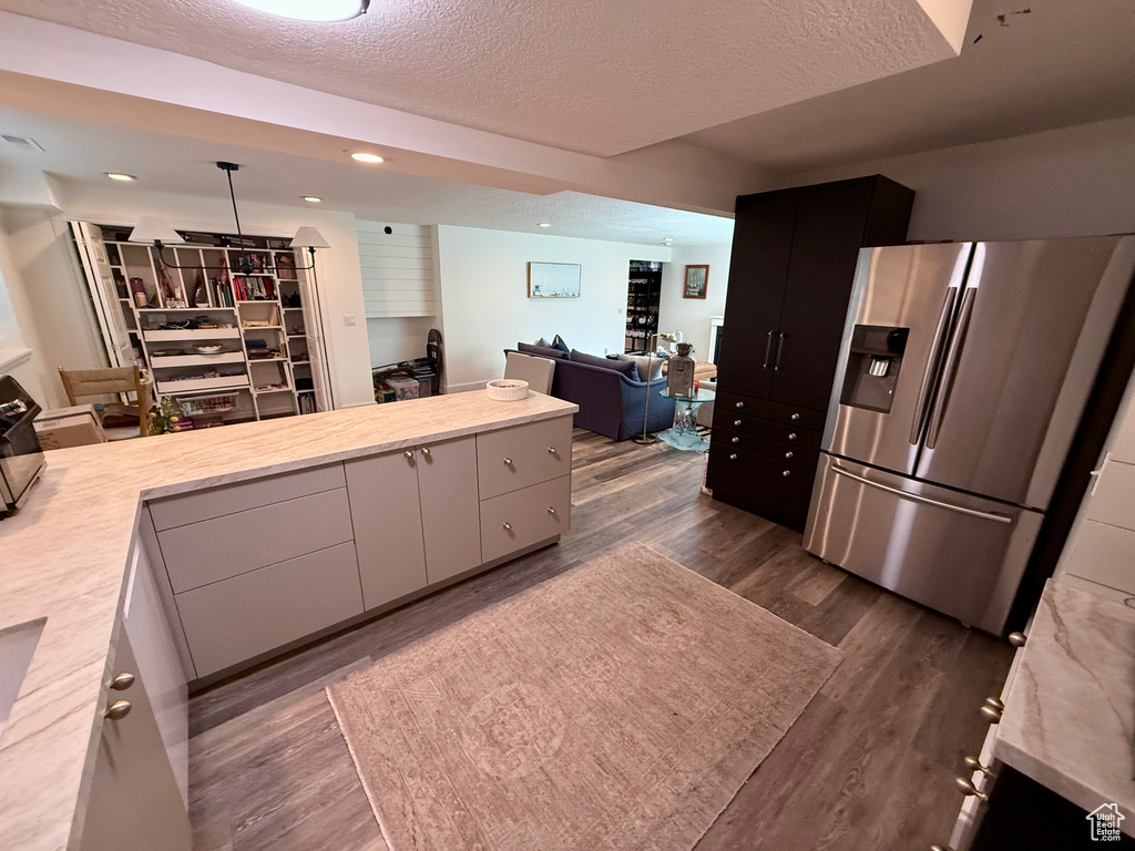 Kitchen with stainless steel refrigerator with ice dispenser, light countertops, a textured ceiling, open floor plan, and dark wood finished floors