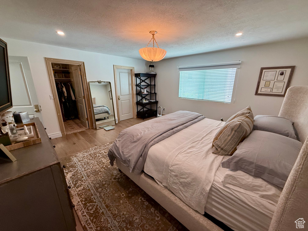 Bedroom with wood finished floors, recessed lighting, a textured ceiling, and a walk in closet
