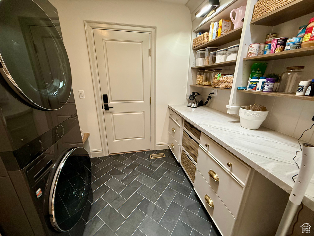 Laundry room with stacked washer and clothes dryer, cabinet space, and baseboards