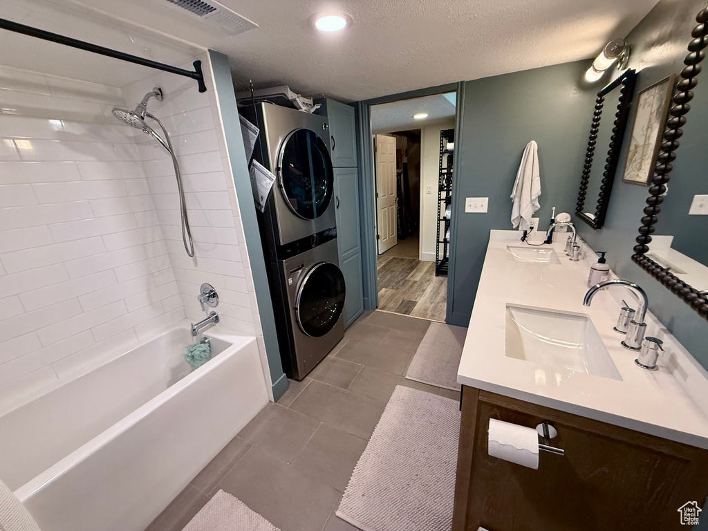 Full bath featuring stacked washer / dryer, double vanity, shower / bath combination, and tile patterned flooring