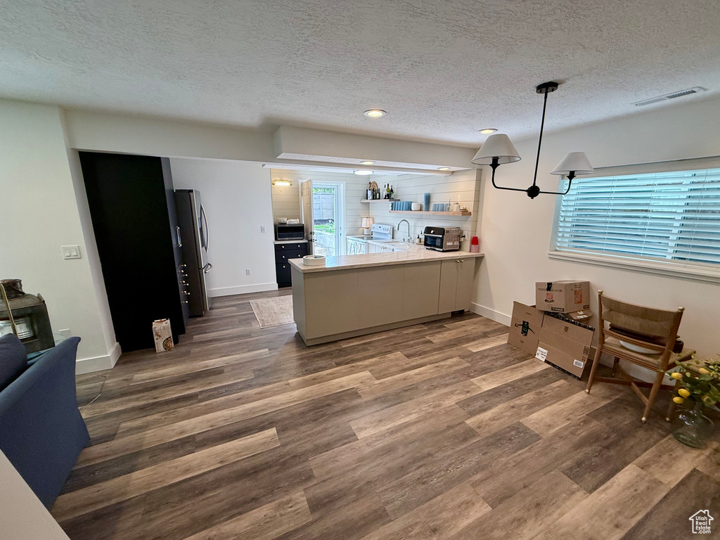 Kitchen with a peninsula, appliances with stainless steel finishes, a textured ceiling, wood finished floors, and open shelves