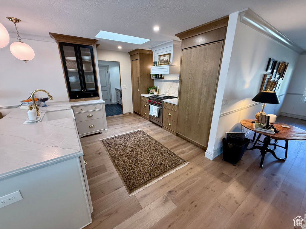 Kitchen with stainless steel range, a skylight, light wood-style flooring, glass insert cabinets, and light countertops