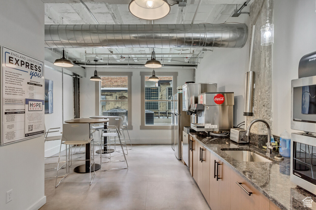 Kitchen with a sink, dark stone countertops, stainless steel microwave, baseboards, and finished concrete floors