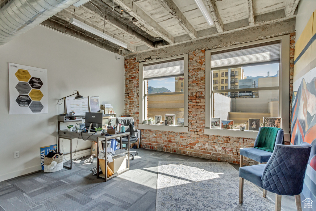 Carpeted home office featuring brick wall