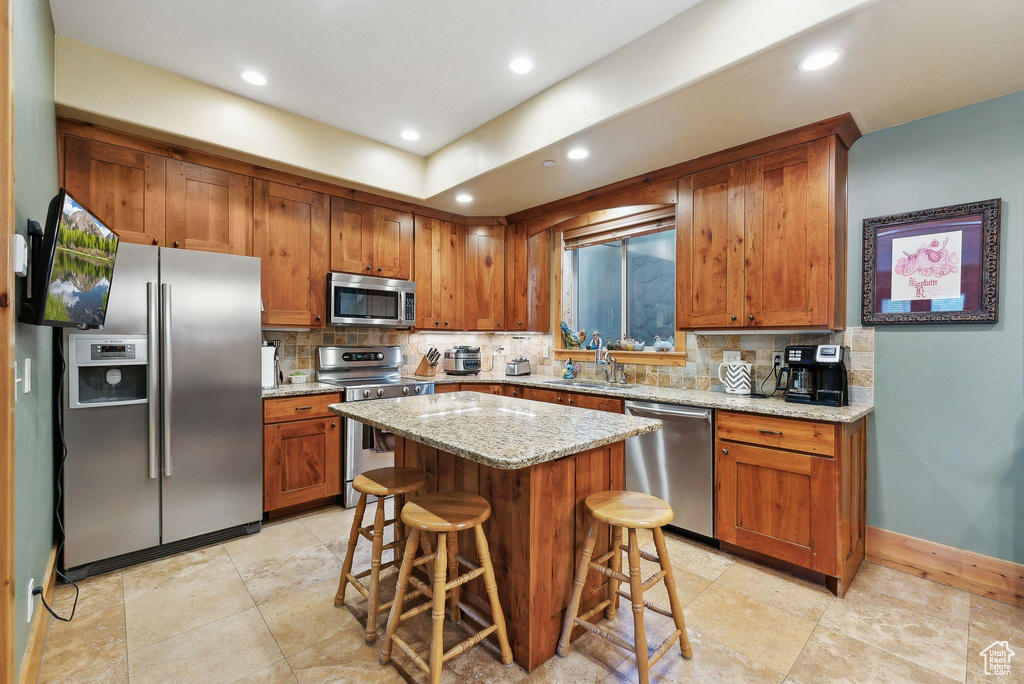 Kitchen with appliances with stainless steel finishes, brown cabinets, a kitchen breakfast bar, decorative backsplash, and recessed lighting