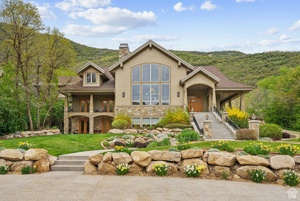 View of front of house featuring stairway, a chimney, a balcony, a front lawn, and stone siding