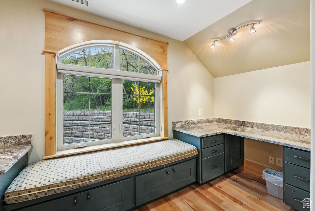 Unfurnished office with light wood finished floors, vaulted ceiling, and built in desk