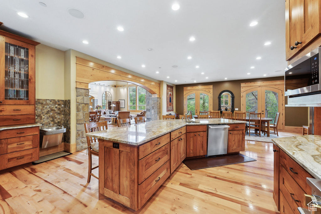 Kitchen with arched walkways, appliances with stainless steel finishes, french doors, a breakfast bar area, and light wood finished floors
