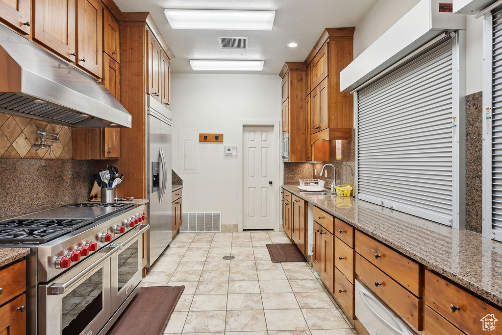 Kitchen featuring appliances with stainless steel finishes, under cabinet range hood, brown cabinetry, a sink, and backsplash