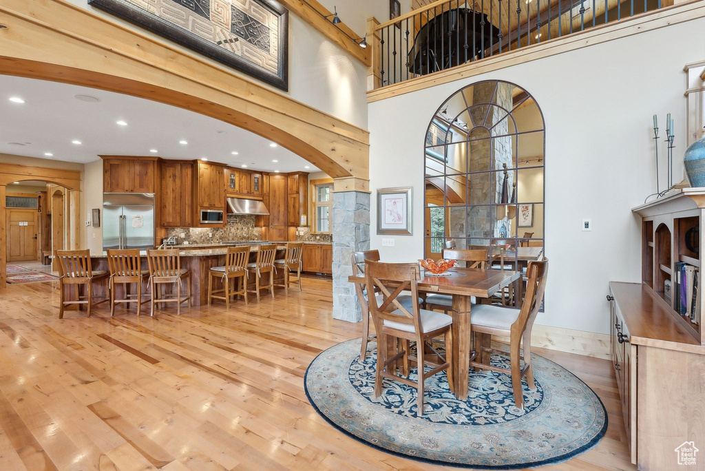 Dining space with arched walkways, recessed lighting, light wood-type flooring, and a high ceiling