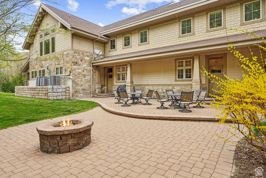 Rear view of property with stone siding, a fire pit, a patio area, and a yard