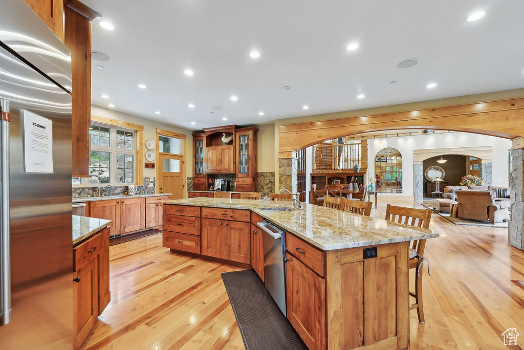 Kitchen with a sink, light wood finished floors, a breakfast bar area, stainless steel dishwasher, and arched walkways