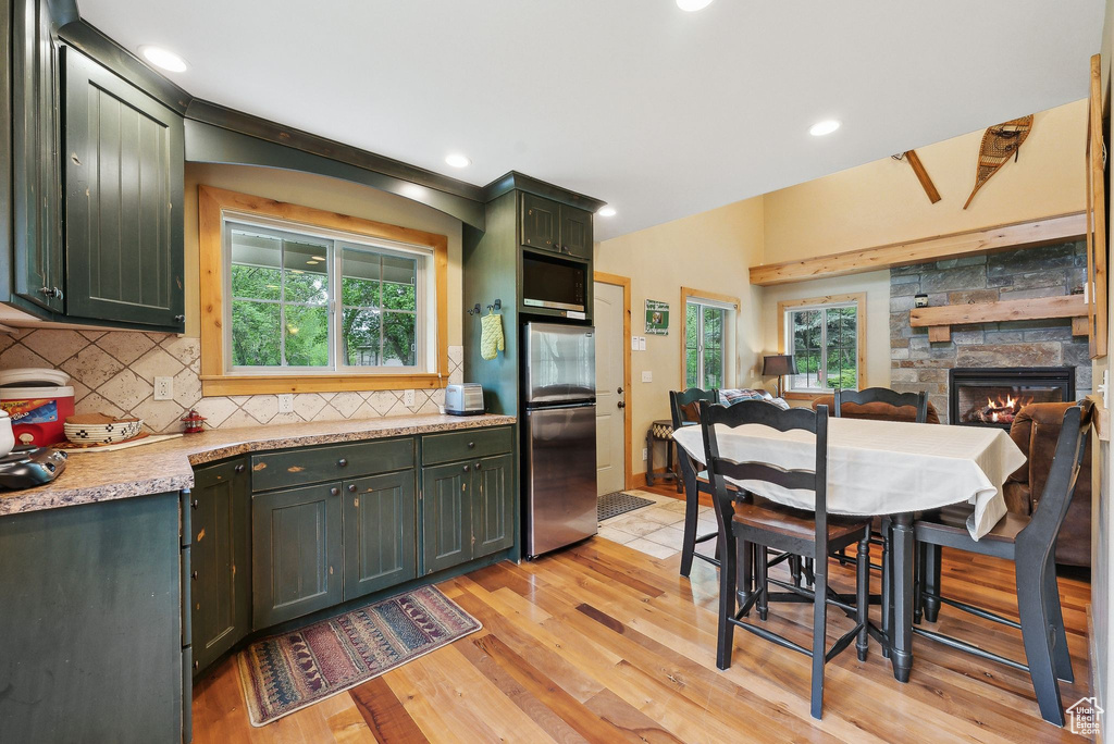 Kitchen featuring appliances with stainless steel finishes, green cabinets, decorative backsplash, light wood-type flooring, and plenty of natural light