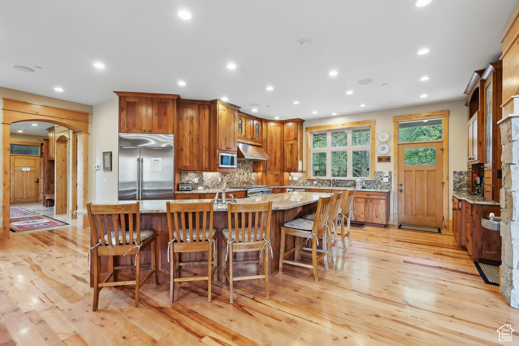 Kitchen with built in appliances, under cabinet range hood, arched walkways, light wood-style flooring, and recessed lighting