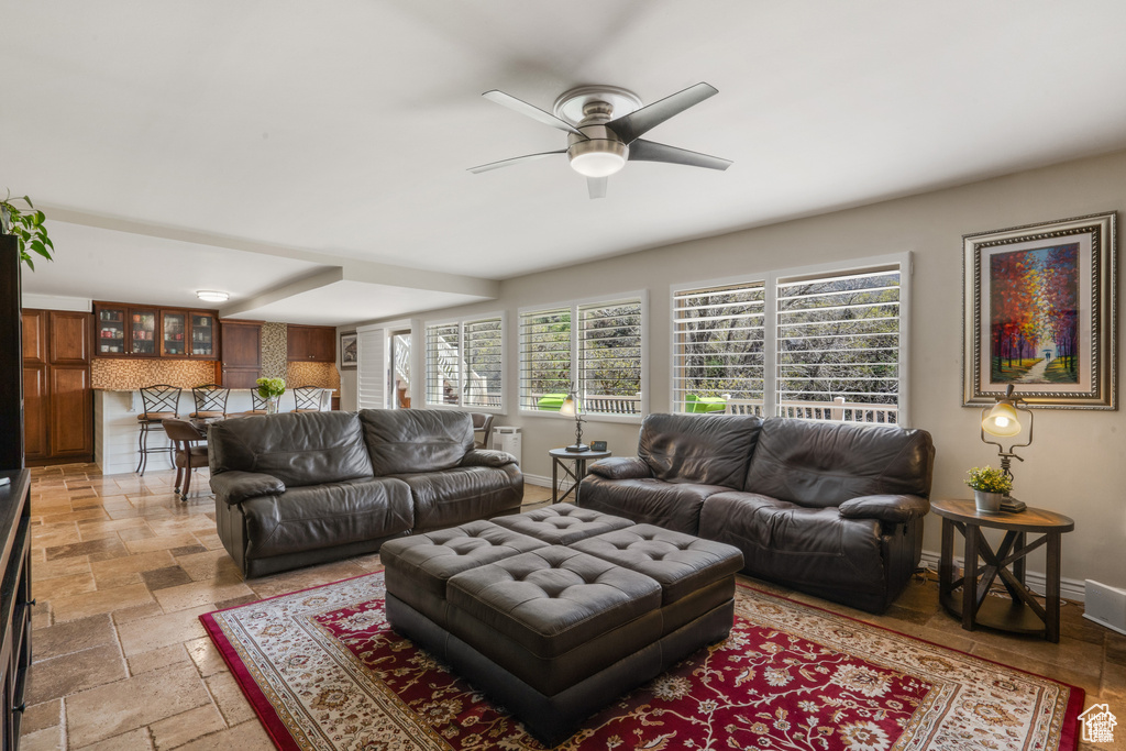 Living area with plenty of natural light, a ceiling fan, baseboards, and stone tile flooring