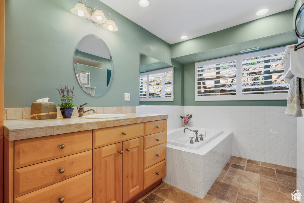 Full bath featuring stone tile flooring, vanity, a bath, and recessed lighting
