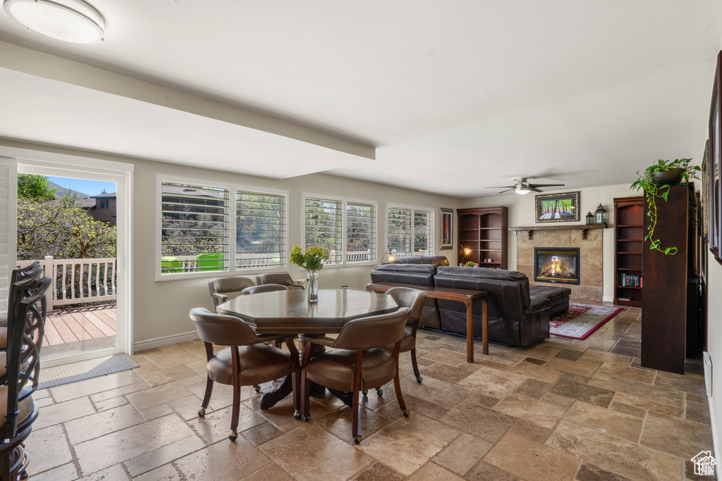 Dining room featuring stone tile floors, ceiling fan, a fireplace, and baseboards