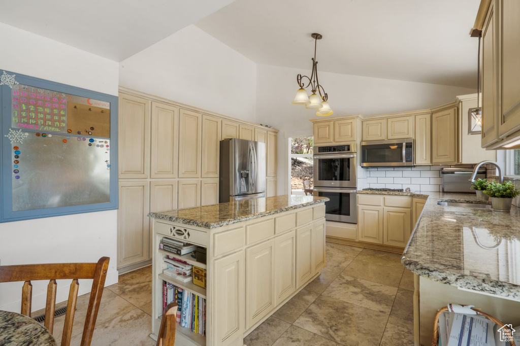 Kitchen with appliances with stainless steel finishes, a sink, vaulted ceiling, cream cabinetry, and light stone countertops