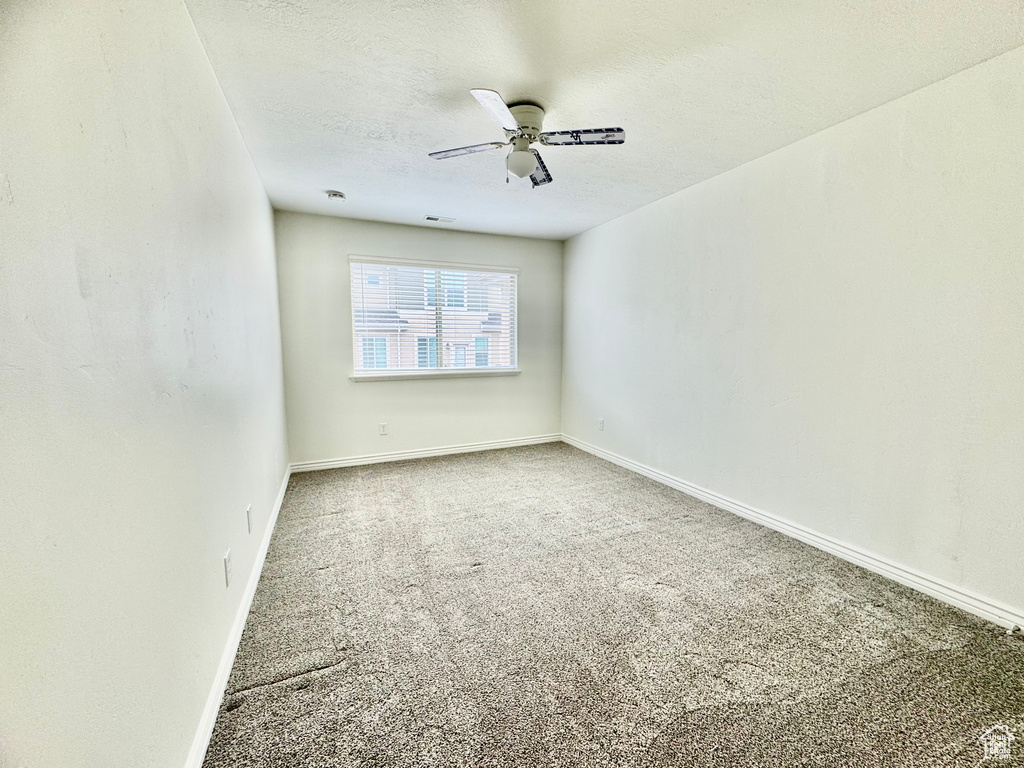 Carpeted spare room with ceiling fan, a textured ceiling, and baseboards