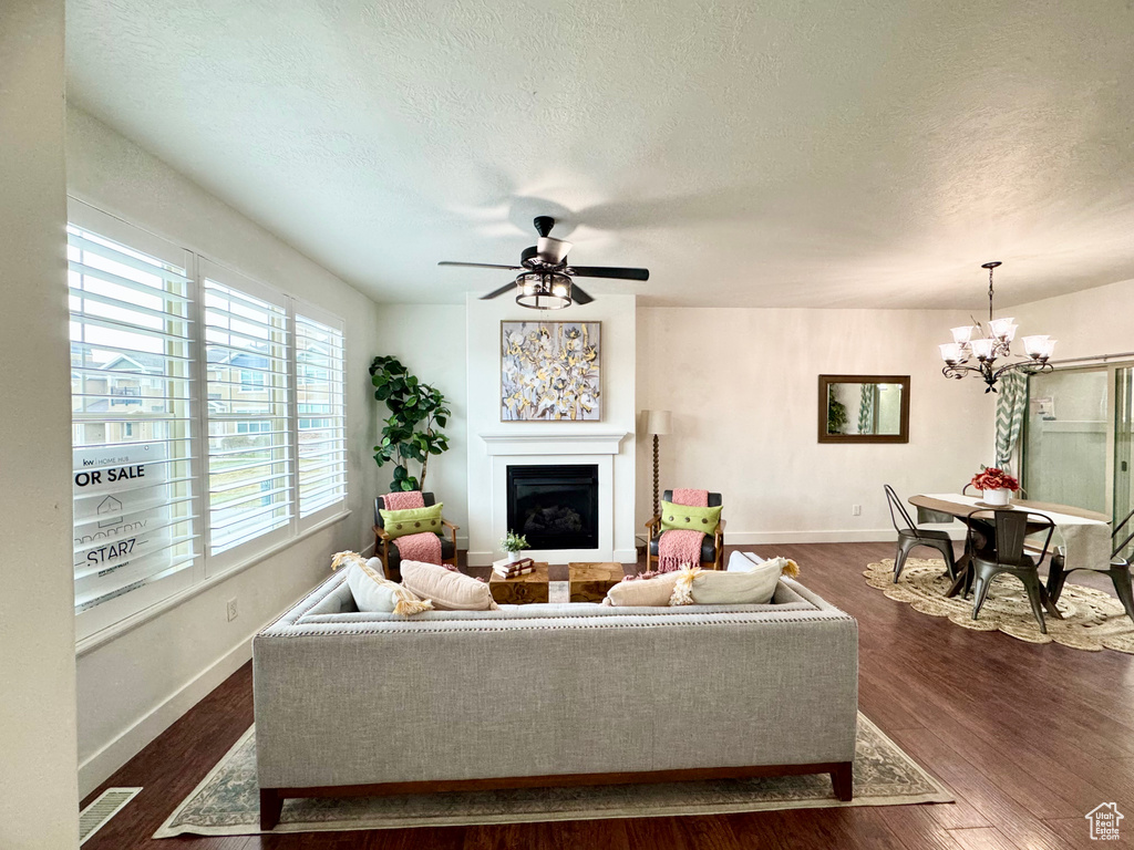 Living area with a chandelier, a fireplace, a textured ceiling, dark wood-type flooring, and baseboards