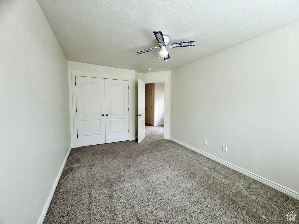 Unfurnished bedroom with carpet, baseboards, a closet, a textured ceiling, and a ceiling fan