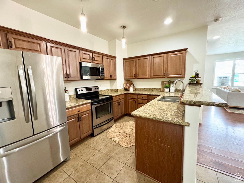 Kitchen with stainless steel appliances, a sink, a peninsula, hanging light fixtures, and brown cabinets