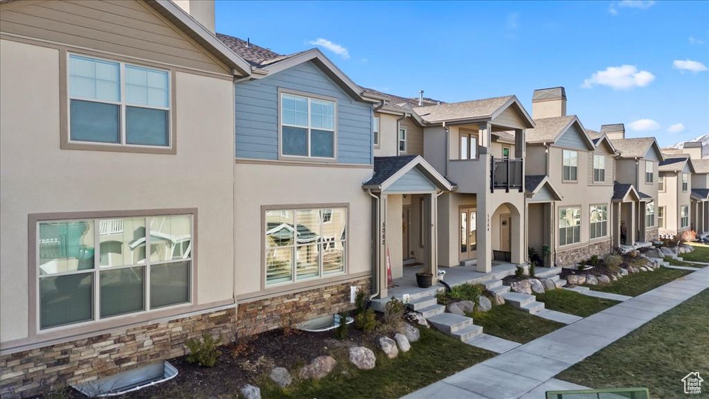 View of property featuring a residential view, stone siding, stucco siding, a chimney, and a balcony