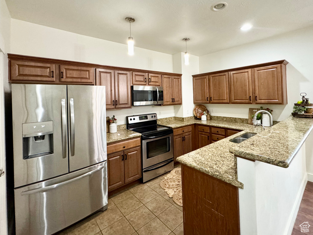 Kitchen featuring appliances with stainless steel finishes, a sink, a peninsula, decorative light fixtures, and brown cabinets