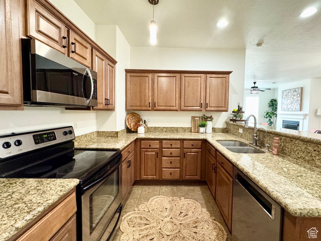 Kitchen featuring appliances with stainless steel finishes, a sink, brown cabinets, a peninsula, and ceiling fan