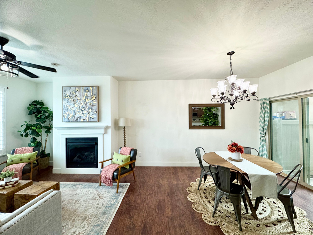 Dining room featuring a chandelier, a fireplace, ceiling fan, baseboards, and wood finished floors