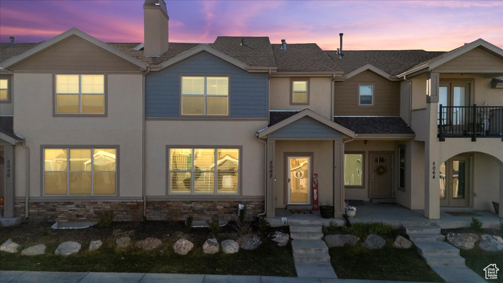 View of front of home featuring a balcony, stucco siding, a chimney, covered porch, and a shingled roof