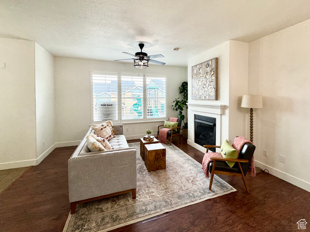 Living area featuring baseboards, wood finished floors, a fireplace, ceiling fan, and a textured ceiling