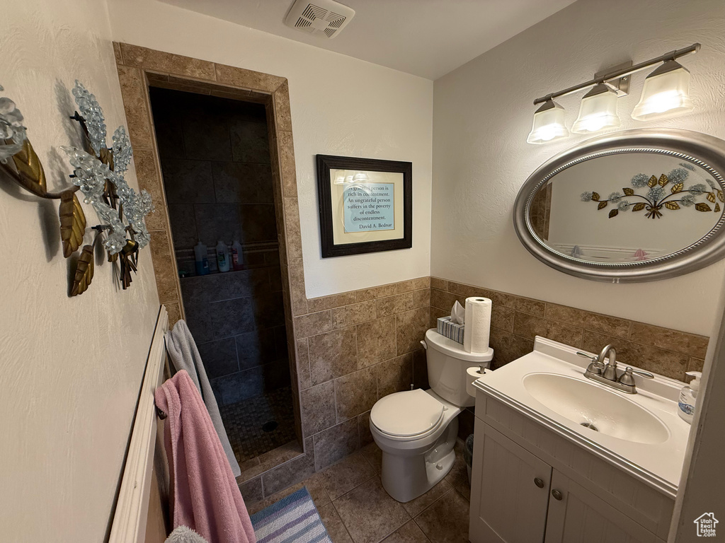 Full bathroom featuring vanity, tiled shower, tile patterned flooring, toilet, and wainscoting