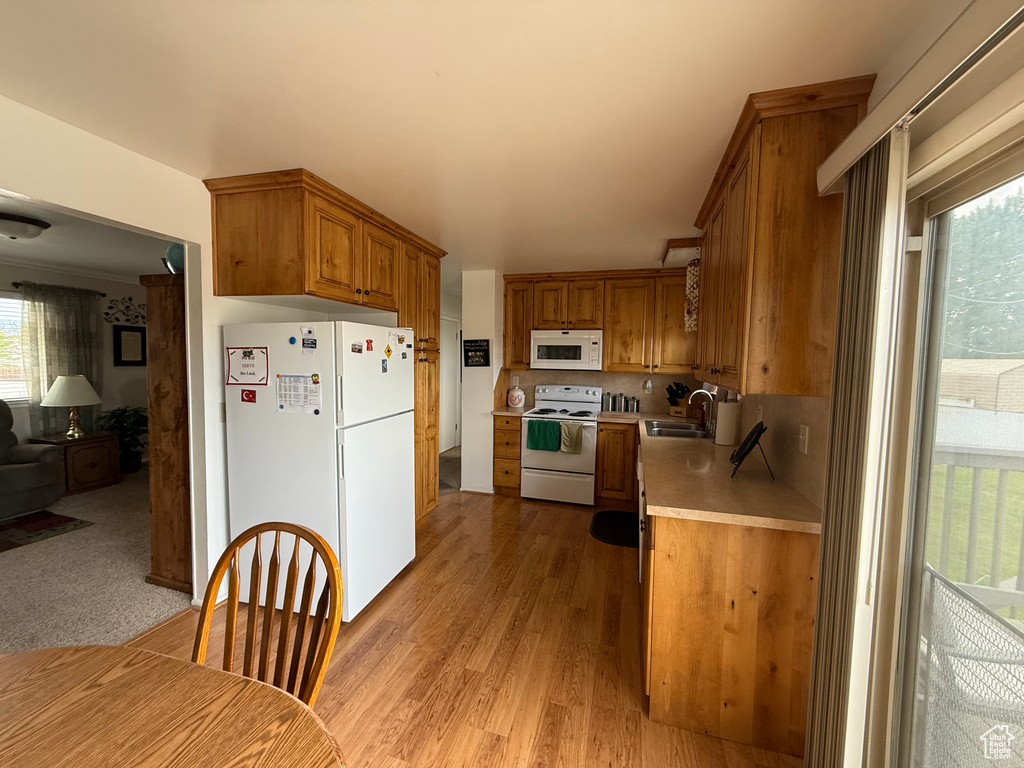 Kitchen with white appliances, a sink, light countertops, brown cabinetry, and light wood-style floors