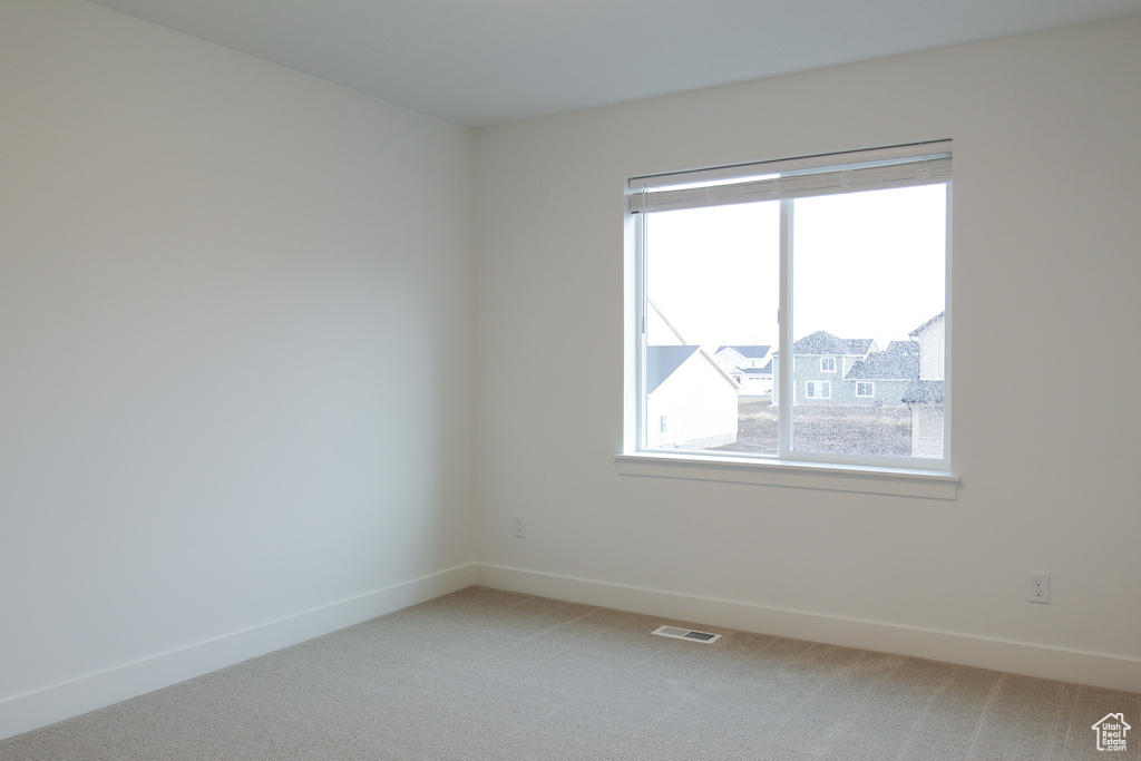 Spare room featuring healthy amount of natural light, light carpet, and baseboards