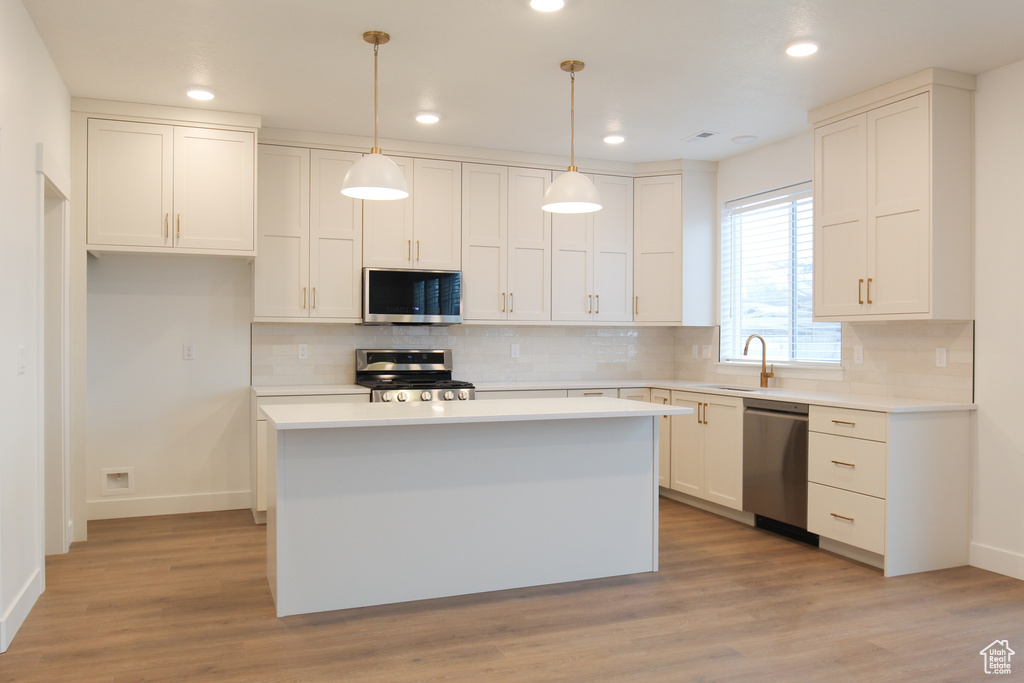 Kitchen featuring appliances with stainless steel finishes, baseboards, white cabinetry, backsplash, and a sink