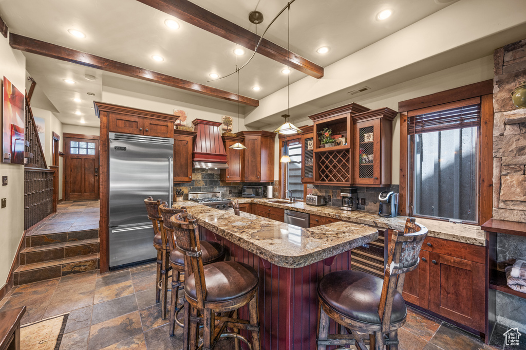 Kitchen with stainless steel appliances, stone tile floors, backsplash, beamed ceiling, and a center island