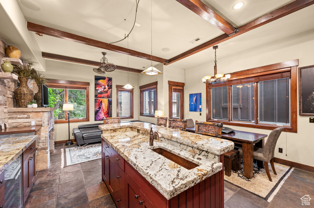 Kitchen with beam ceiling, stone tile floors, a chandelier, and light stone counters