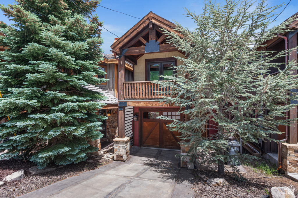 View of front of property featuring driveway, a garage, french doors, a balcony, and stone siding