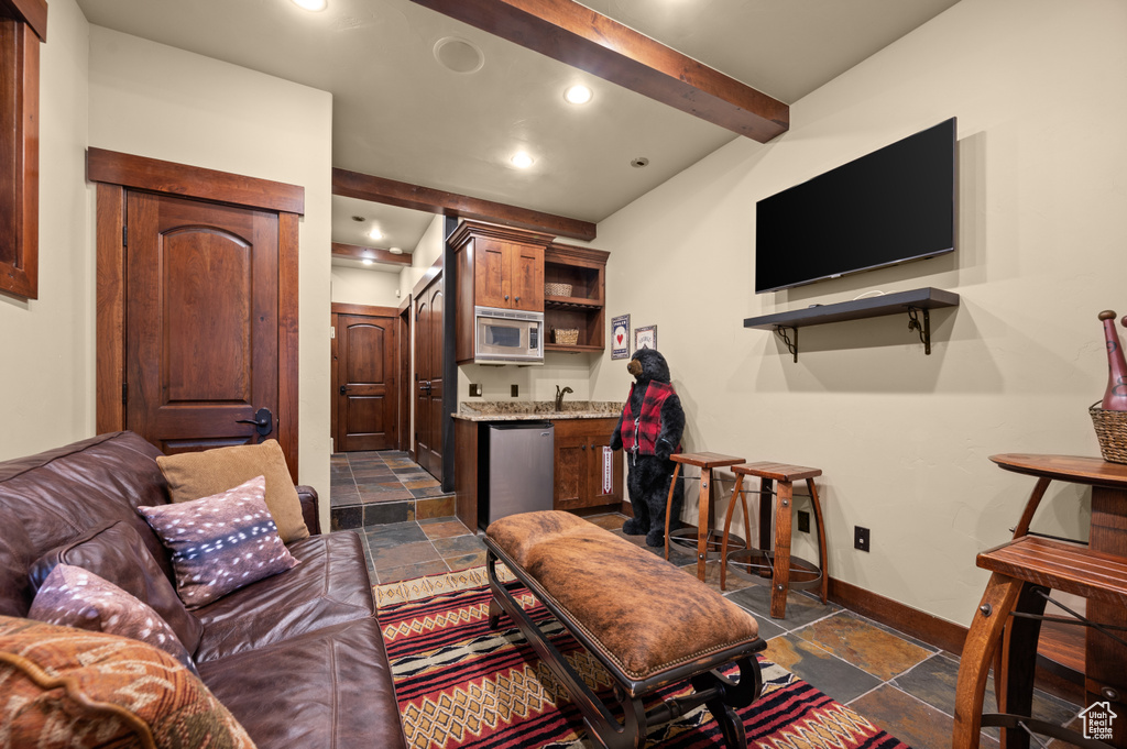 Living area featuring stone tile flooring, bar with sink, recessed lighting, and beamed ceiling