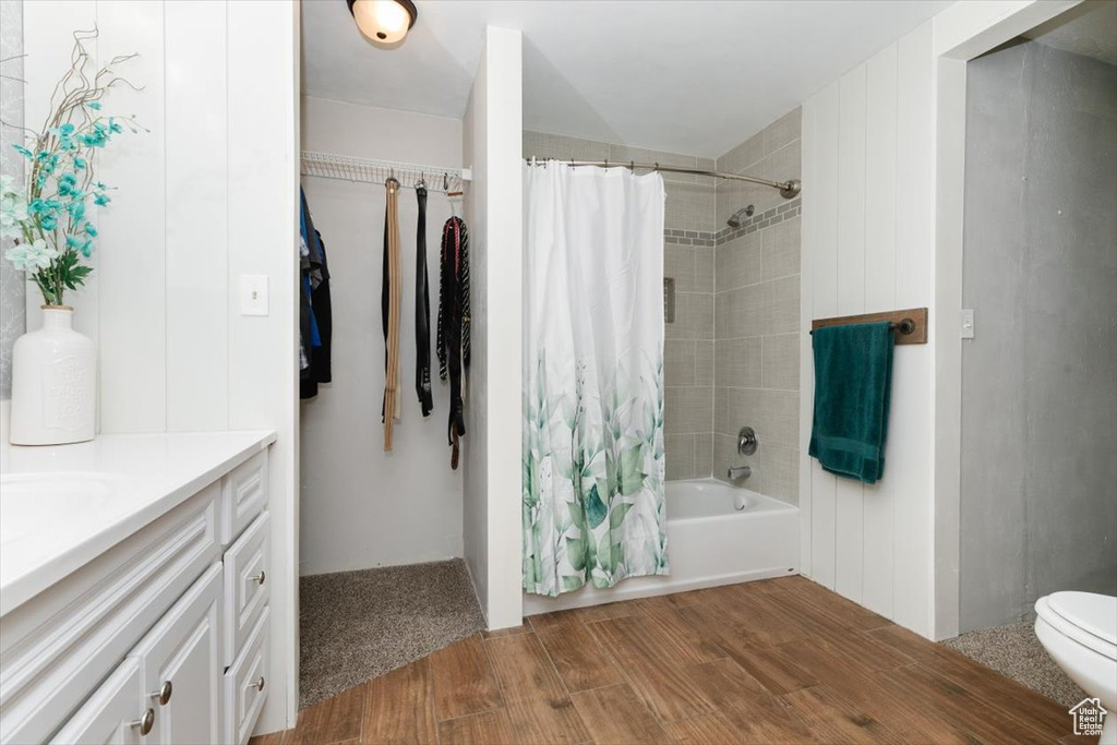 Bathroom with wood finished floors, shower / tub combo with curtain, vanity, and toilet