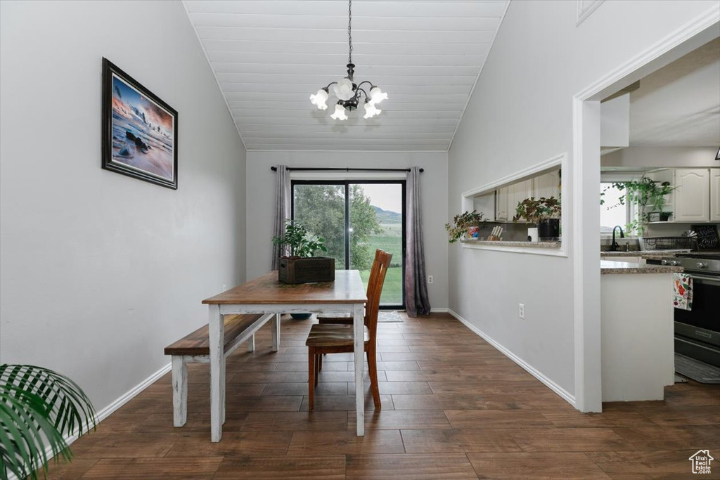 Dining area featuring a chandelier, vaulted ceiling, dark wood-style floors, and baseboards