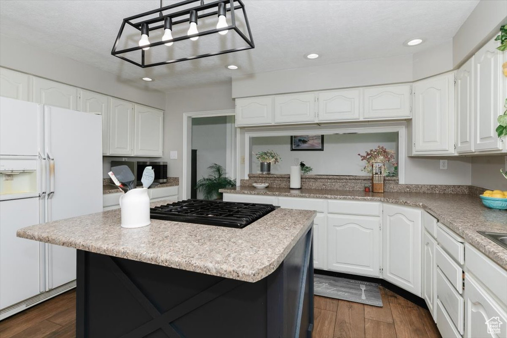 Kitchen featuring white refrigerator with ice dispenser, a kitchen island, stovetop, dark wood-style flooring, and recessed lighting