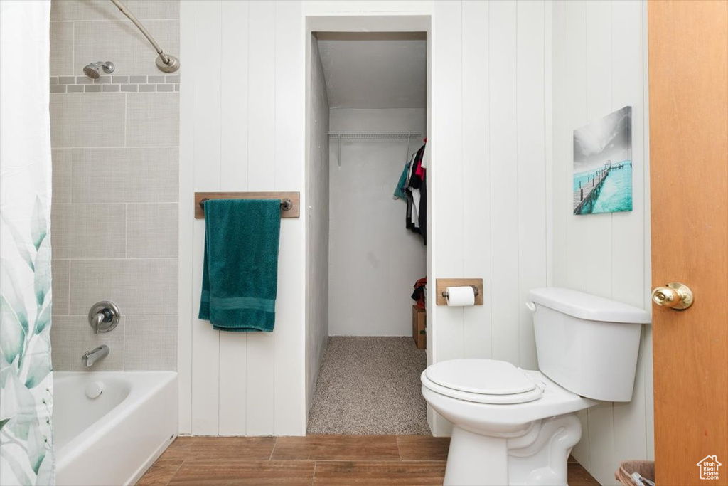 Bathroom with toilet, shower / tub combo with curtain, and wood finished floors