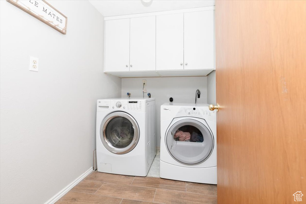 Washroom featuring cabinet space, separate washer and dryer, light wood-style floors, and baseboards