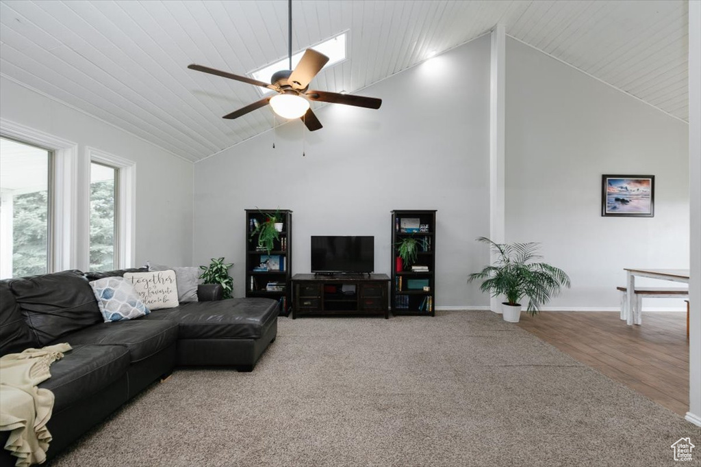 Carpeted living room featuring ceiling fan, high vaulted ceiling, baseboards, and wood finished floors