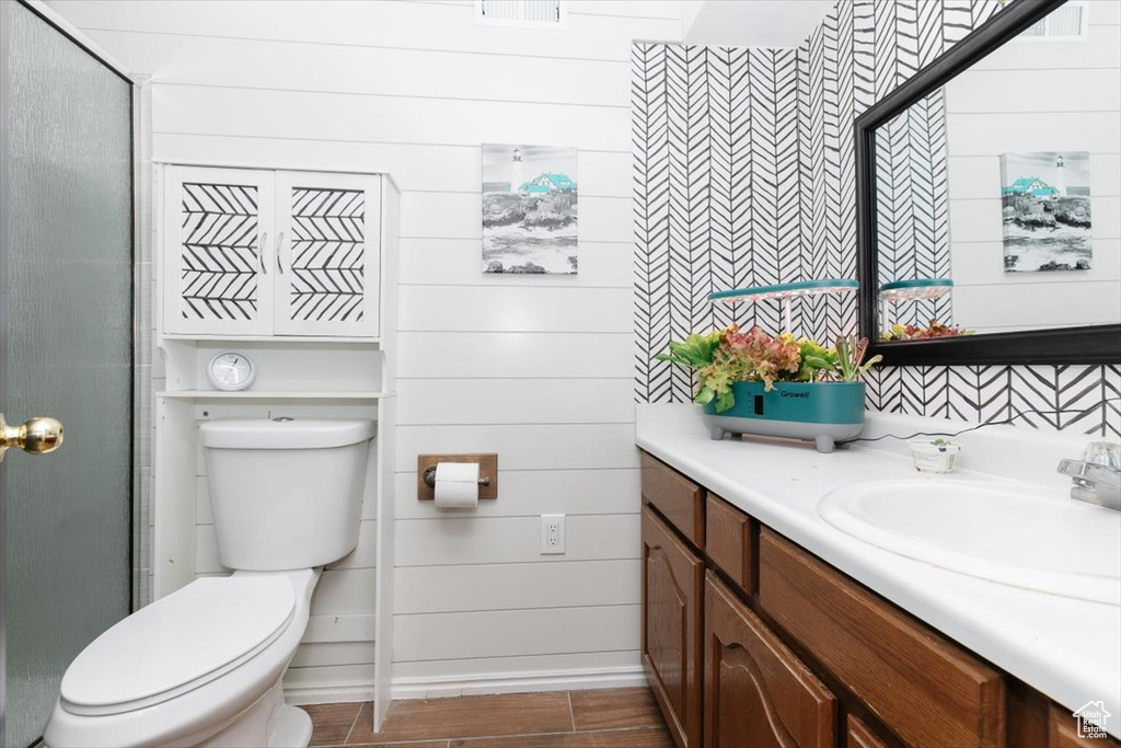 Full bathroom with vanity, toilet, a shower stall, wood finished floors, and wooden walls