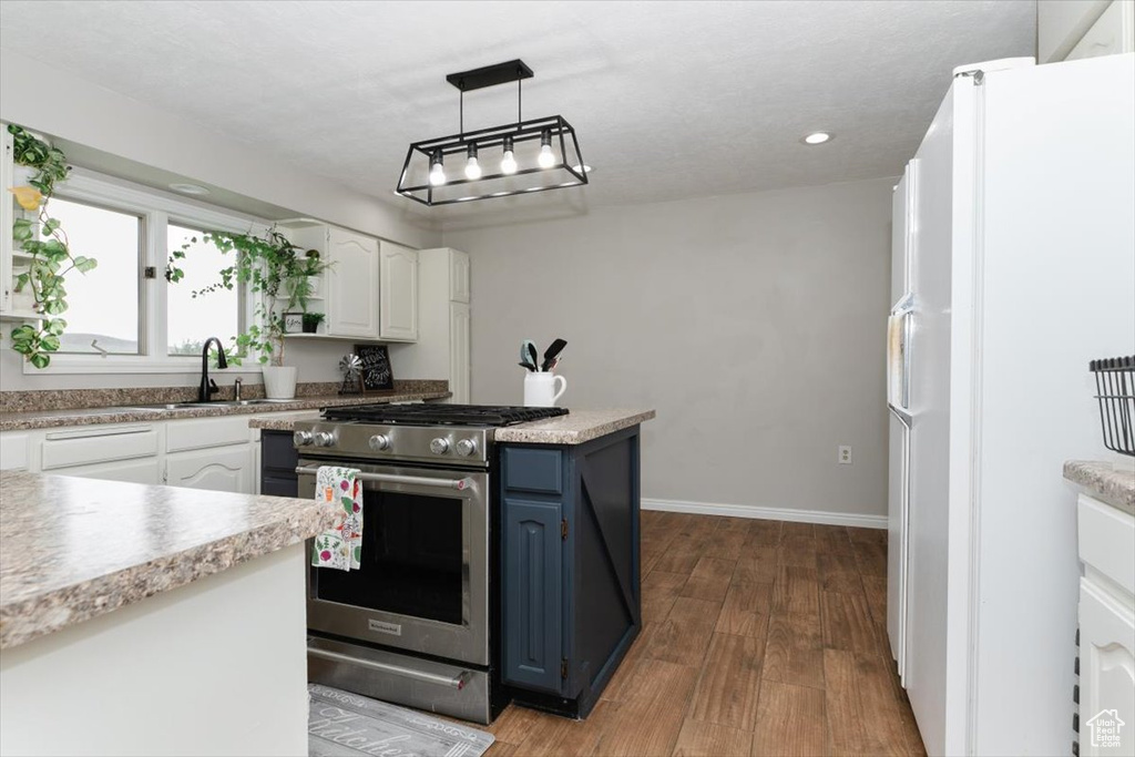 Kitchen featuring freestanding refrigerator, stainless steel range with gas stovetop, a sink, blue cabinetry, and wood finished floors